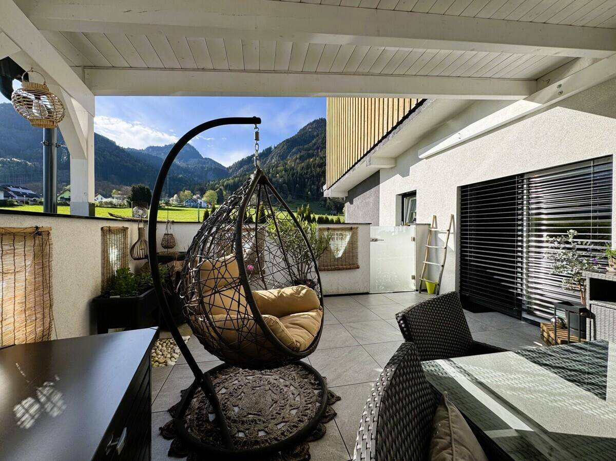 Sonnige Terrasse mit Hängesessel und Blick auf die umliegende Berglandschaft.