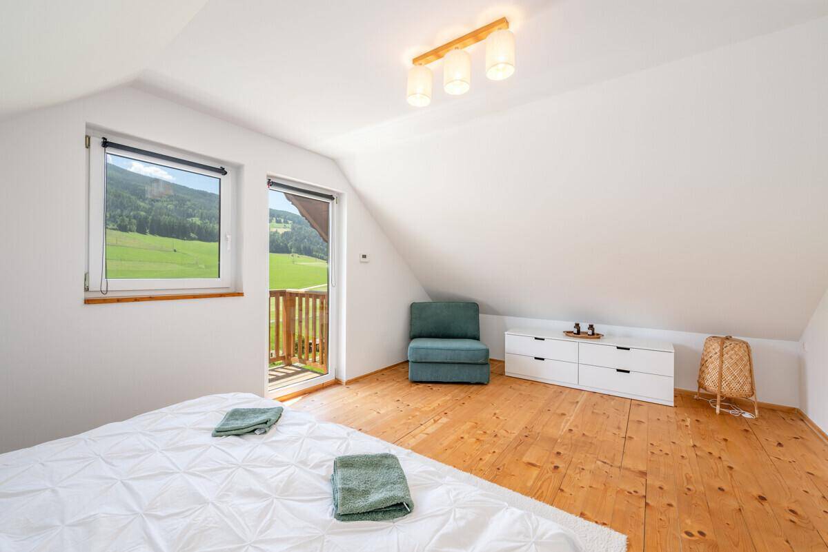 Geräumiges Schlafzimmer im Dachgeschoss mit Holzboden, blauem Sessel und schöner Aussicht.