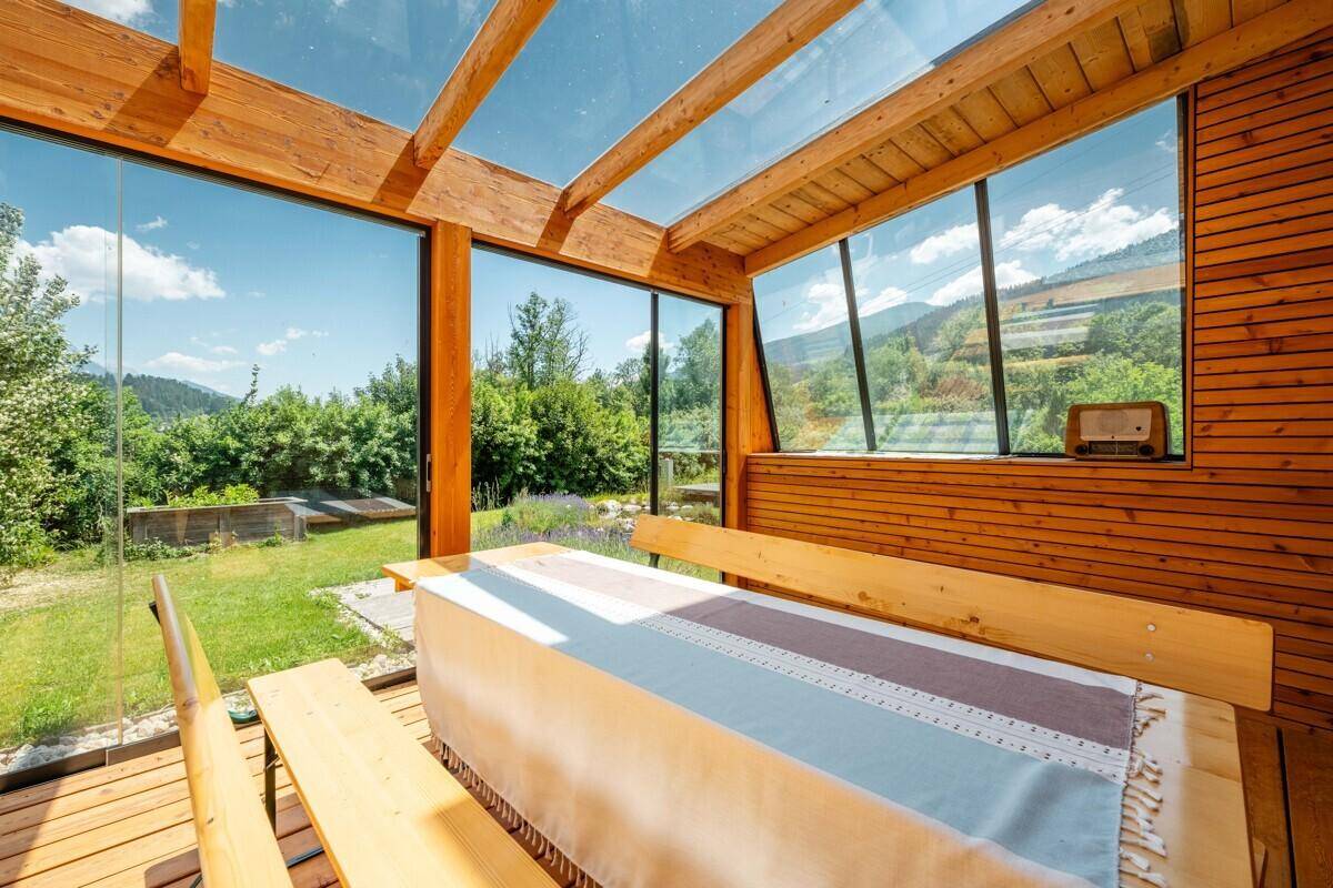 Lichtdurchfluteter Wintergarten mit Panoramablick auf die grüne Landschaft und die Berge.