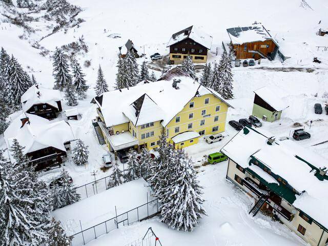 Luftaufnahme des gelben Gebäudes und der Umgebung im Winter, alles mit Schnee bedeckt, inklusive Spielplatz.