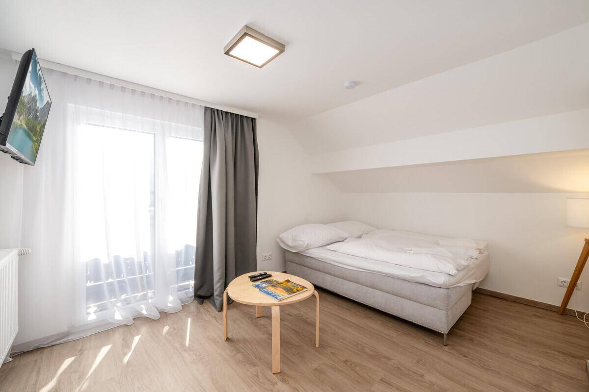 Helles Schlafzimmer mit Einzelbett, kleinem Tisch und Zugang zum Balkon.