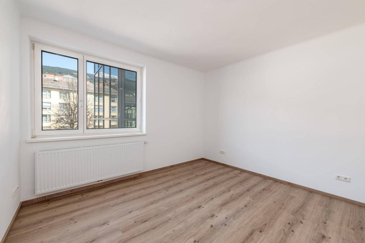 Helles Zimmer mit Holzboden und großen Fenstern, ideal als Schlaf- oder Arbeitszimmer nutzbar.