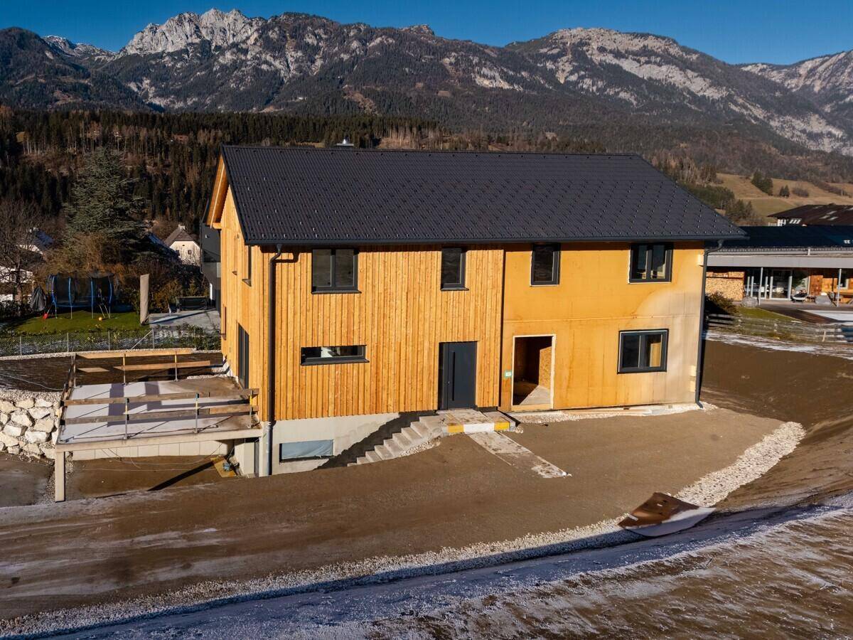 Attraktives Holzhaus mit dunklen Fenstern und Bergblick in sonniger Lage.
