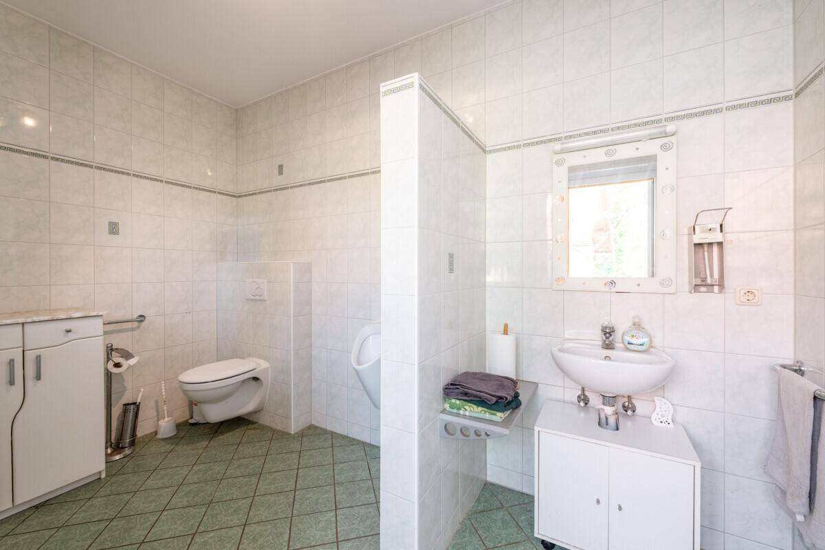 Gefliestes Badezimmer mit WC, Urinal, Waschbecken und Fenster, in hellem Design und gut gepflegt.