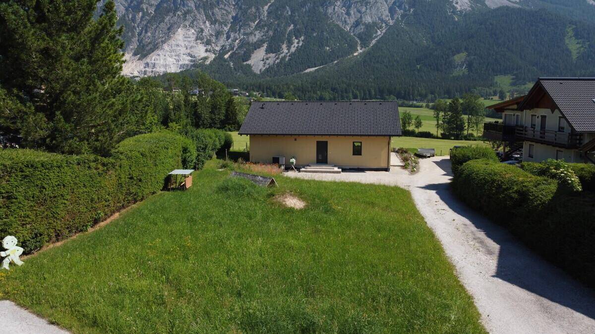 Luftaufnahme eines Hauses und einer Rasenfläche, umgeben von Hecken mit Bergpanorama im Hintergrund.