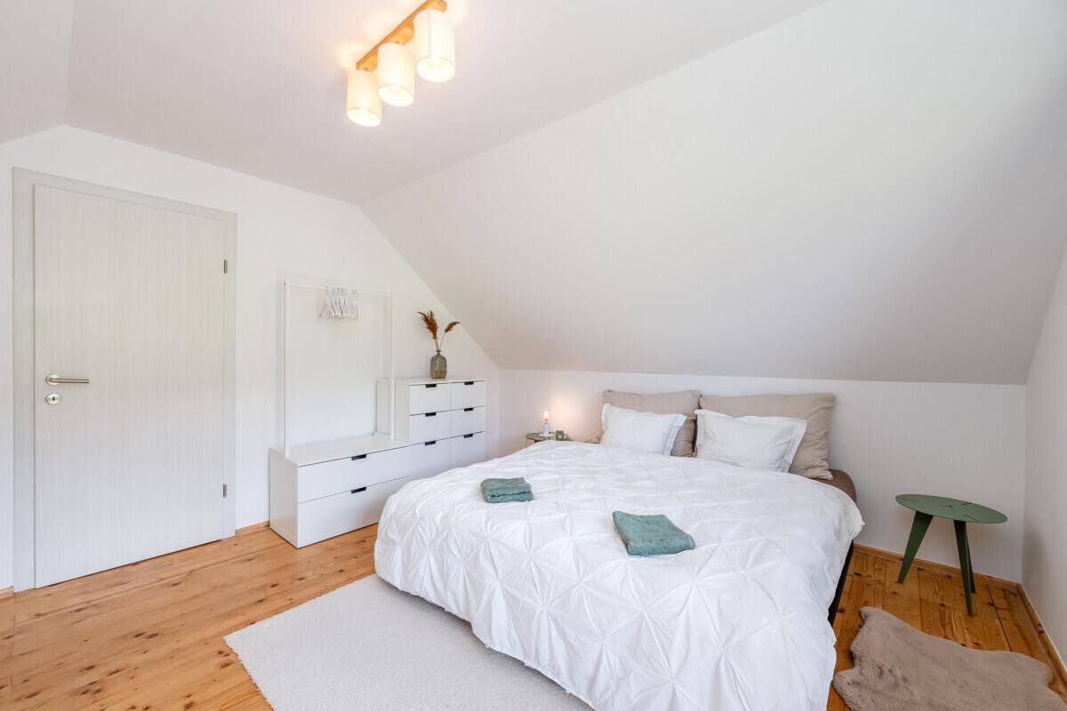 Gemütliches Schlafzimmer im Dachgeschoss mit Holzboden, weißem Bett und modernen Möbeln.