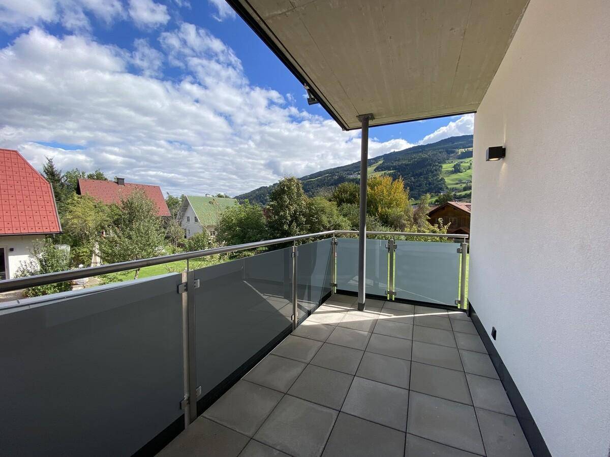 Heller Balkon mit Fliesenboden, Glasgeländer und Panoramablick auf die umliegenden Berge.