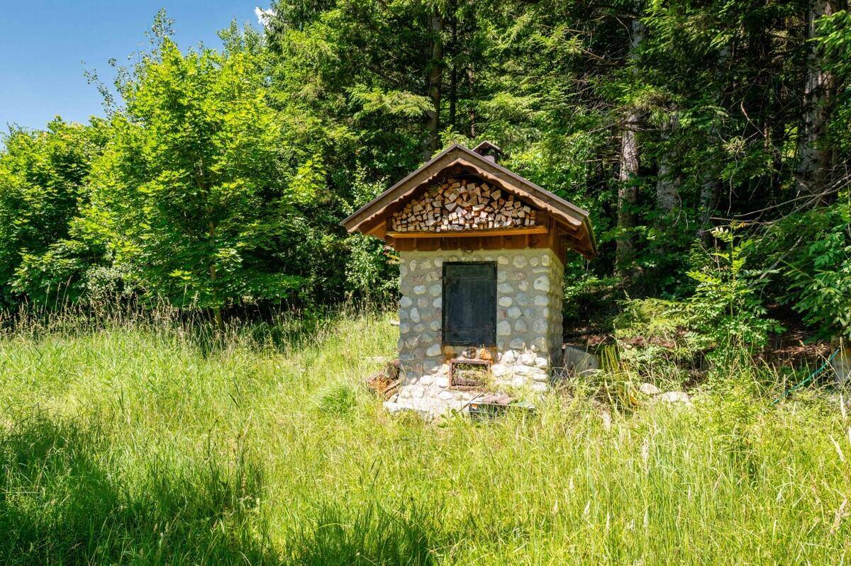 Kleines Steingebäude mit Holzüberdachung und Holzstapel in einer grünen Wiese.