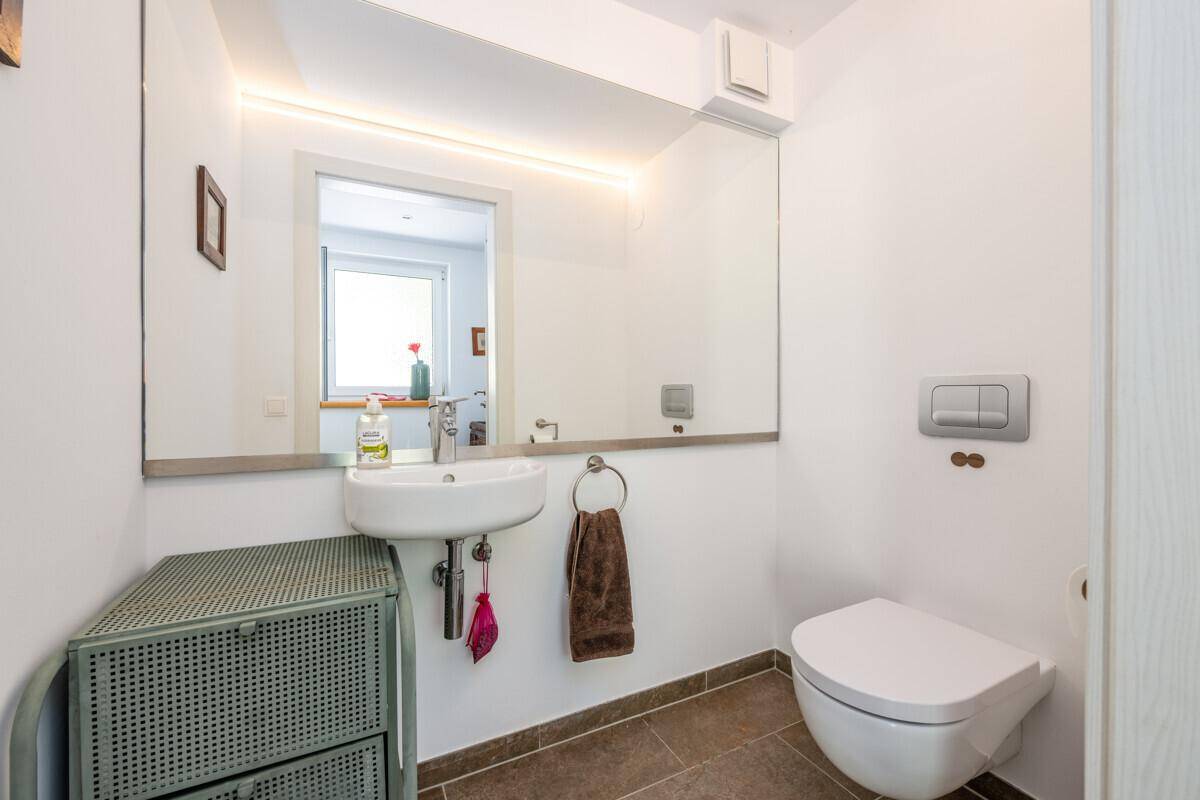 Modernes Gäste-WC mit wandhängender Toilette, Einzelwaschbecken und beleuchtetem Spiegel.