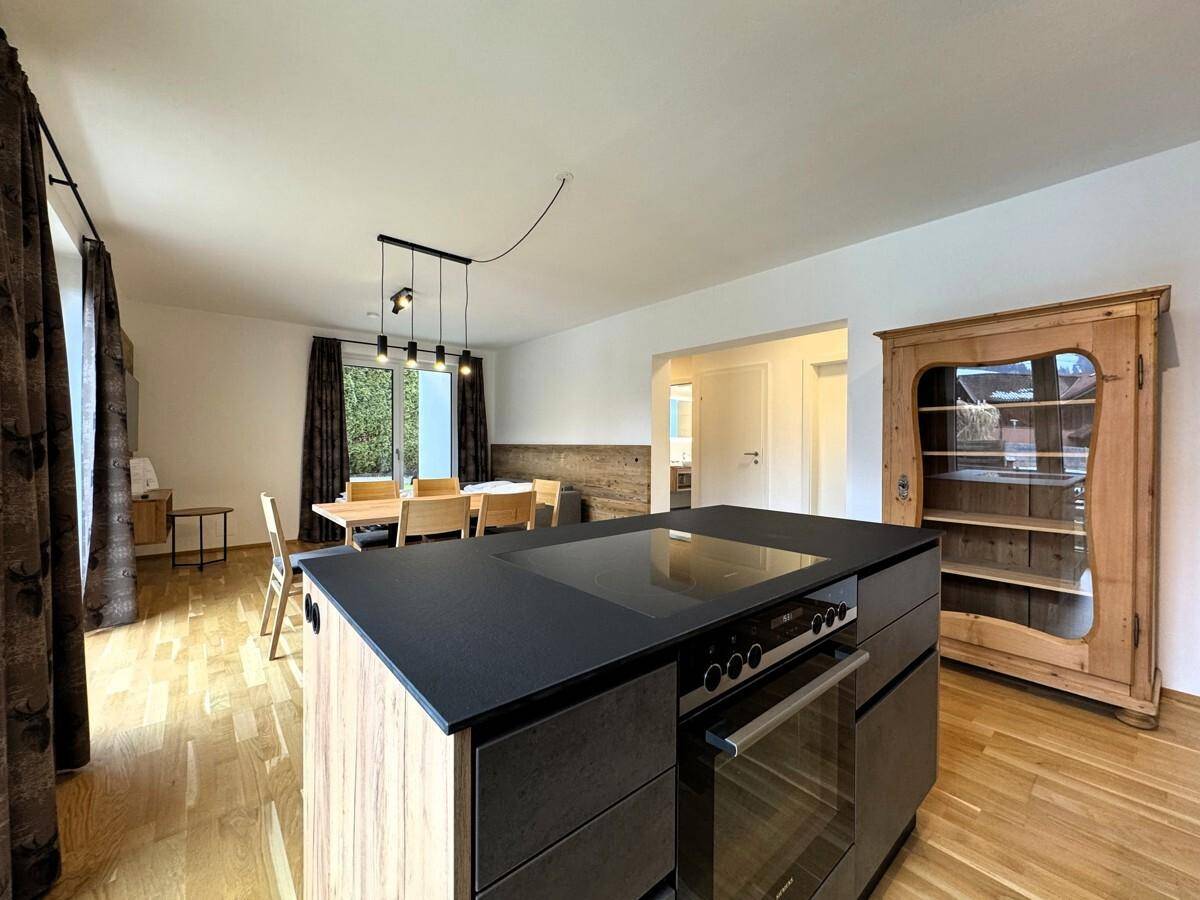 Heller Wohn-Essbereich mit Holztisch, offener Küche und traditionellem Holzschrank.