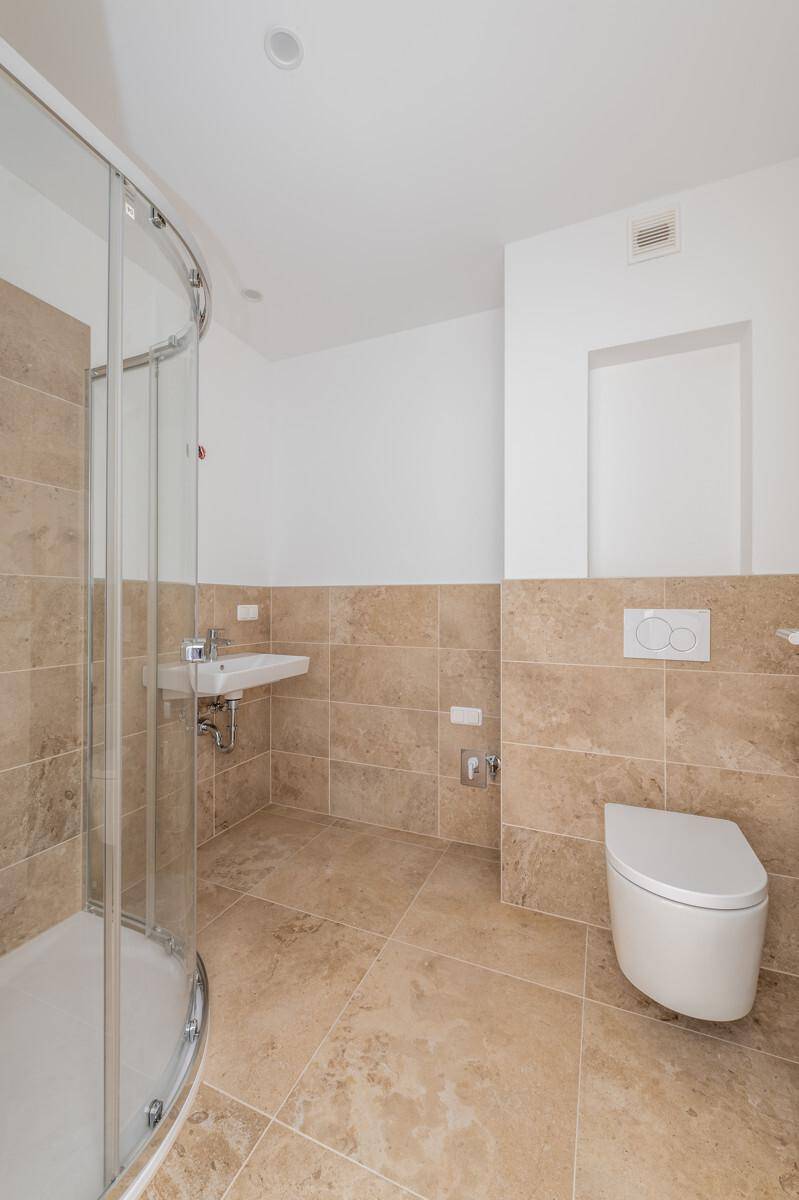 Modernes Badezimmer mit beigefarbenen Fliesen, einer Duschkabine und wandhängendem WC.