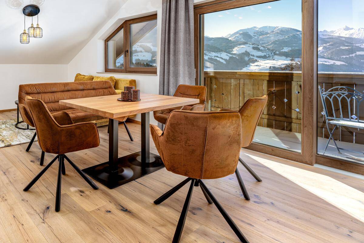 Gemütlicher Essbereich mit Holzboden, Bergblick und Zugang zum Balkon, unter einer Dachschräge.