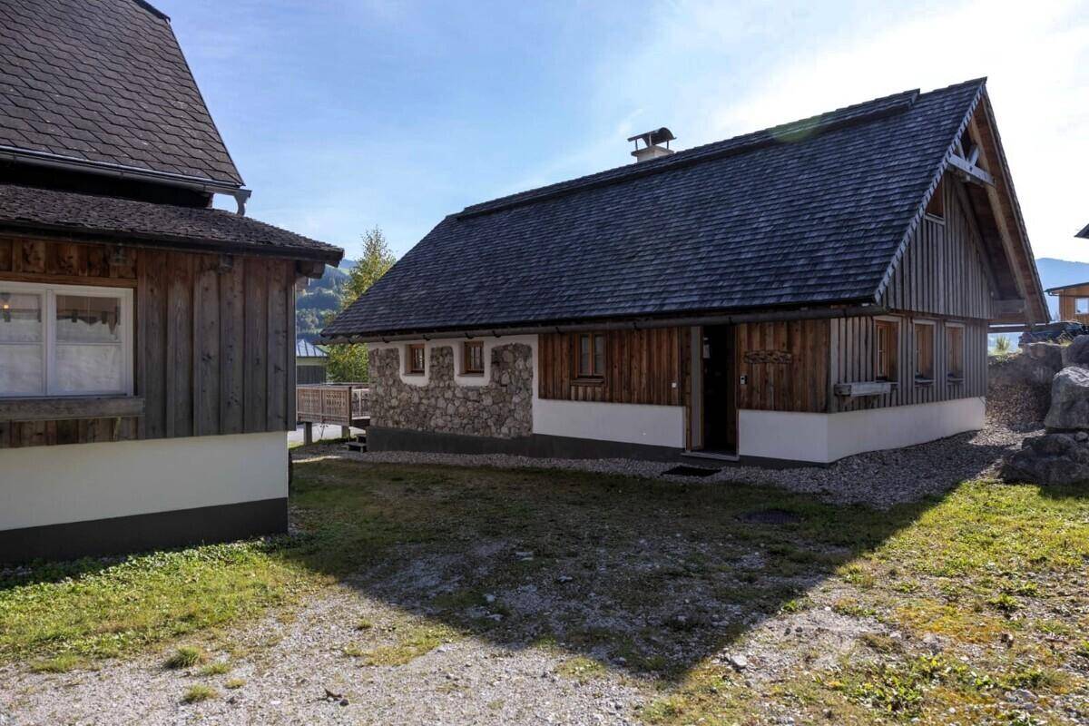 Rustikales Holzhaus mit Steinsockel und Schindeldach, umgeben von einer ländlichen Umgebung.