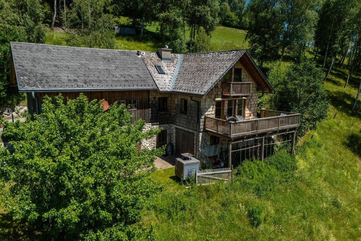 Das Chalet ist eingebettet in eine idyllische grüne Hügellandschaft mit dichtem Wald im Hintergrund.