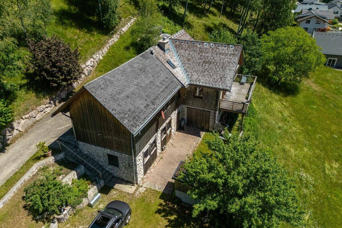 Vogelperspektive des Chalets mit Satteldach, umgeben von grünen Wiesen und Bäumen unter blauem Himmel.