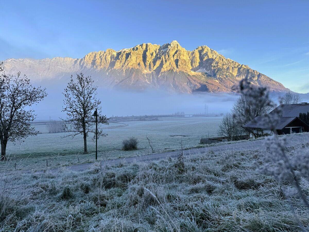 Malerische Winterlandschaft mit majestätischen Bergen, die im Morgenlicht leuchten, und frostbedeckten Feldern.