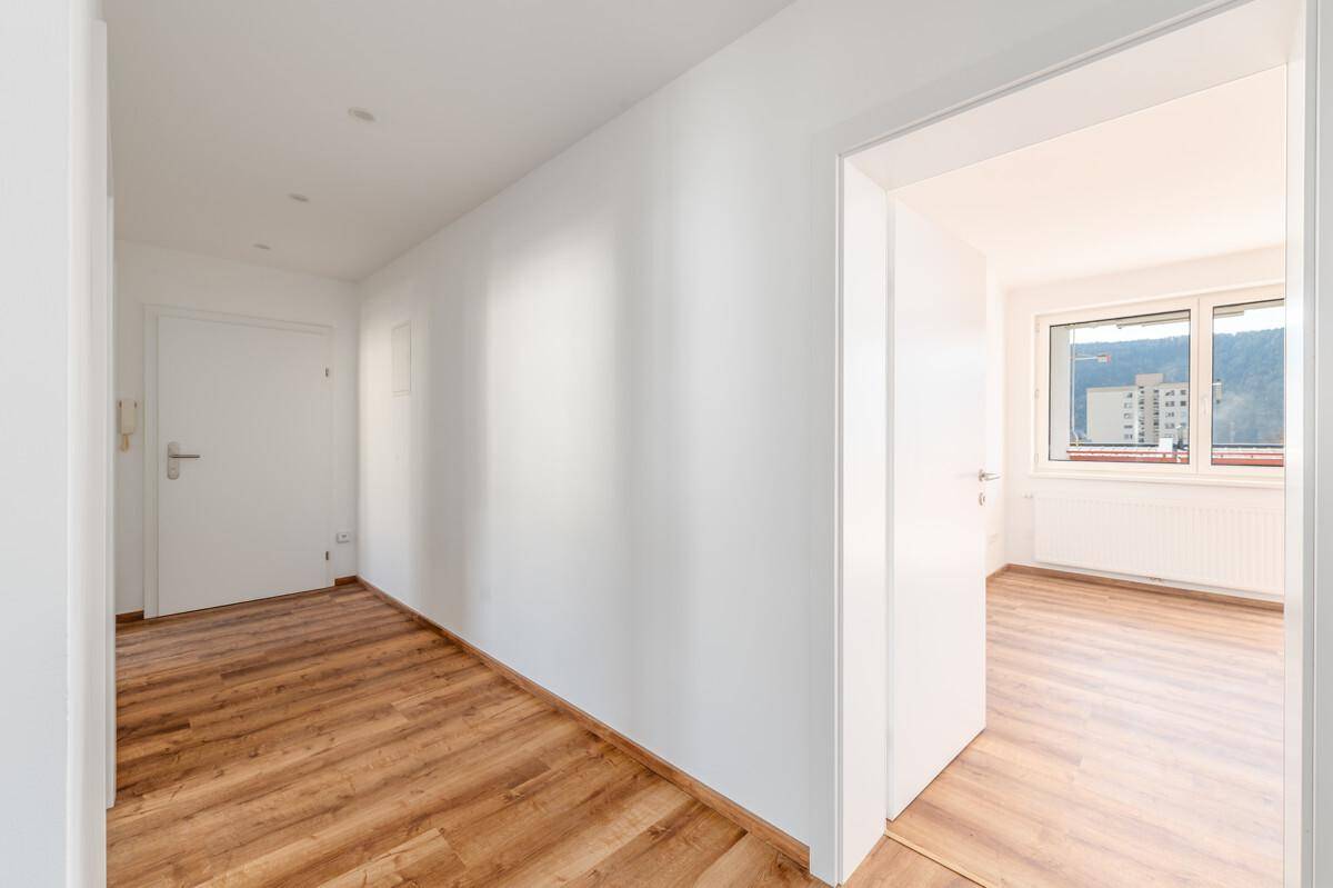 Heller Flur mit Holzboden und weißen Wänden, der zu weiteren Zimmern der Wohnung führt.