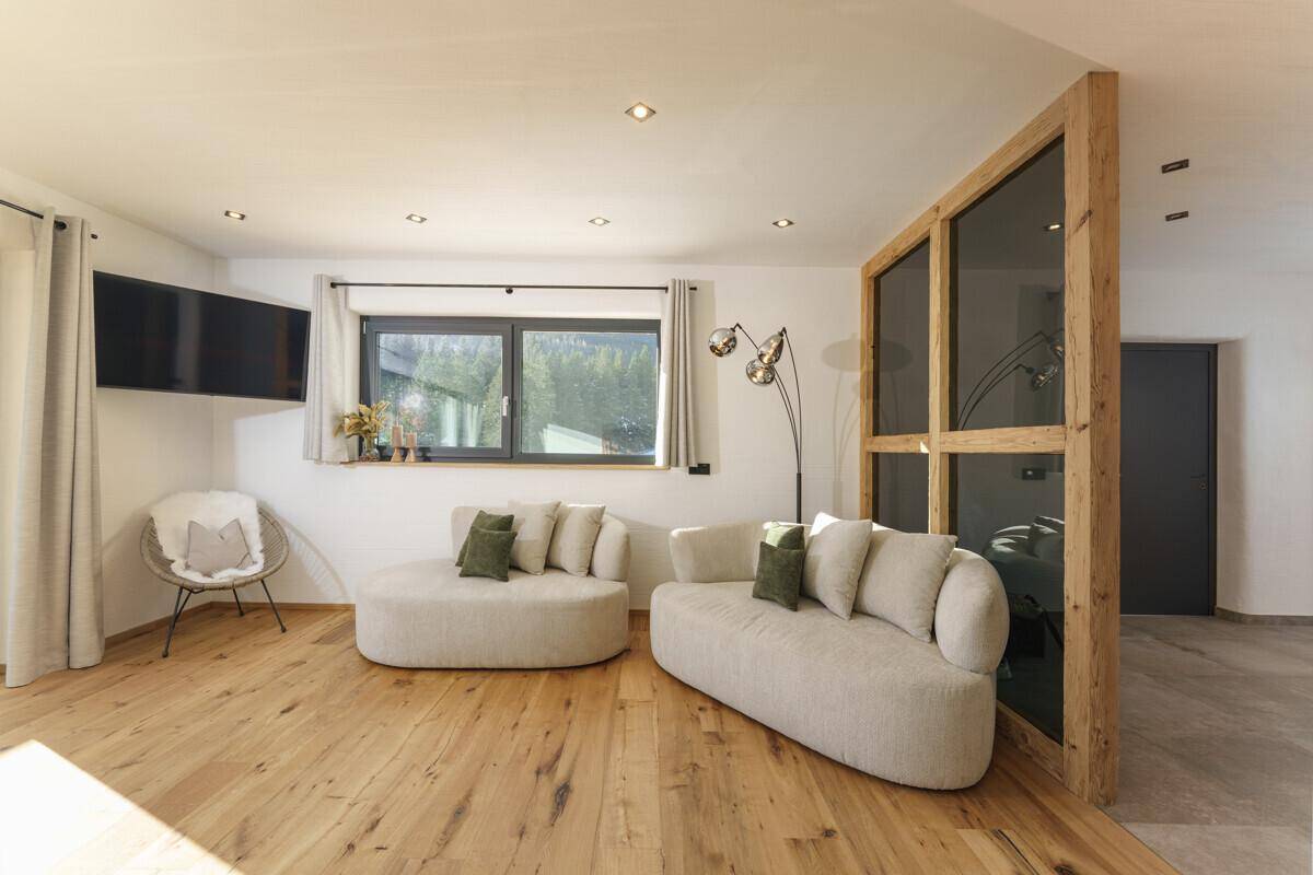 Gemütliches Wohnzimmer mit Holzboden, bequemen Sofas und einem Fenster mit Bergblick.