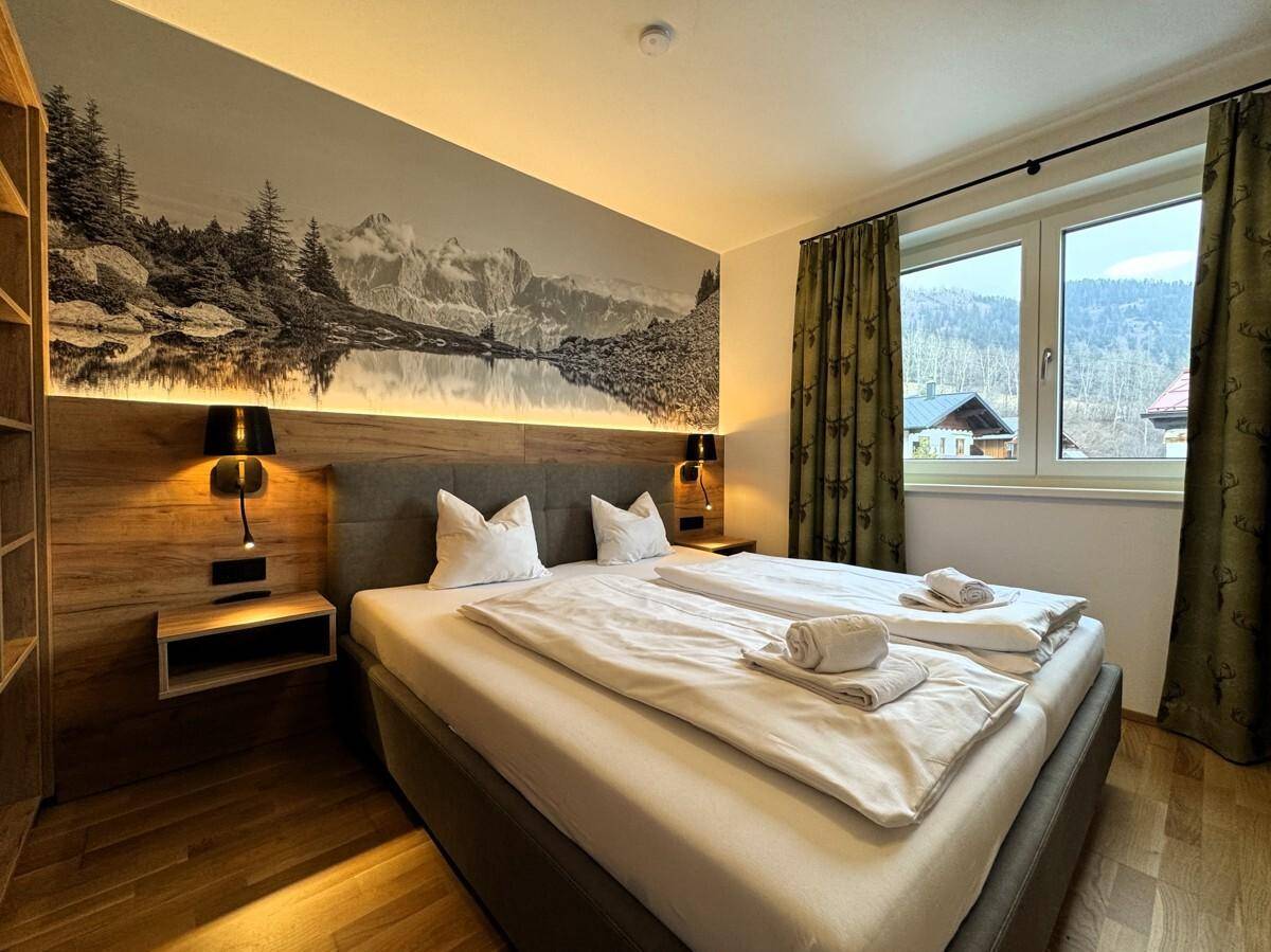 Helles Schlafzimmer mit Doppelbett, Holzboden und Fenster mit Blick auf die Berge.