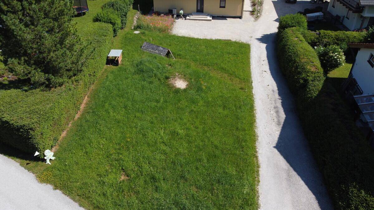 Nahaufnahme aus der Luft eines grünen Grundstücks mit einer kleinen Hütte, umgeben von Hecken und Wegen.