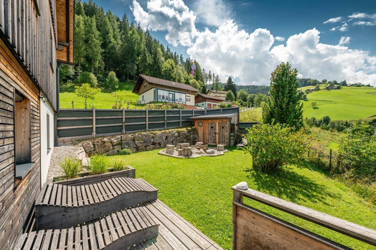 Gepflegter Gartenbereich mit Rasen, Holzsitzgelegenheiten und einem kleinen Schuppen in Hanglage.
