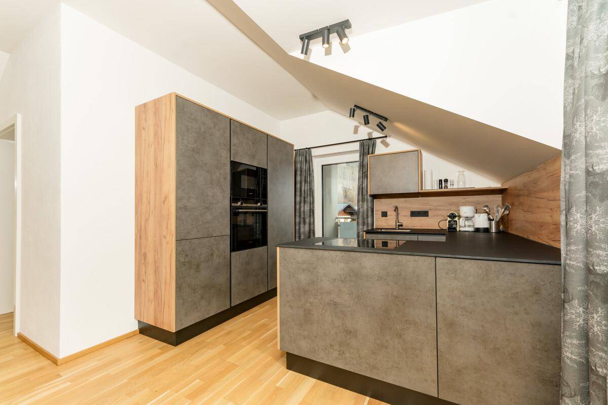 Moderne Einbauküche mit dunklen Fronten, integrierten Geräten und Dachschräge.