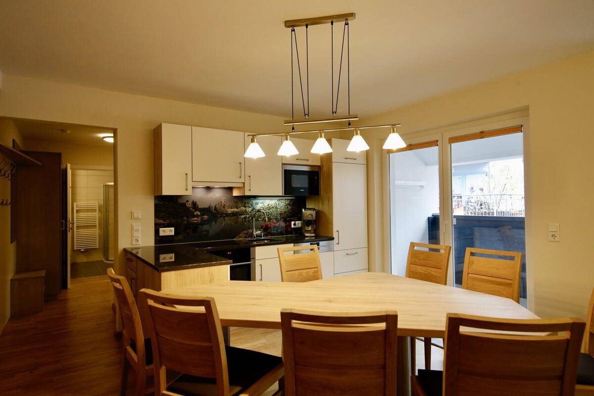 Heller Essbereich mit großem Holztisch, modernen Pendelleuchten und Zugang zu einem Balkon.