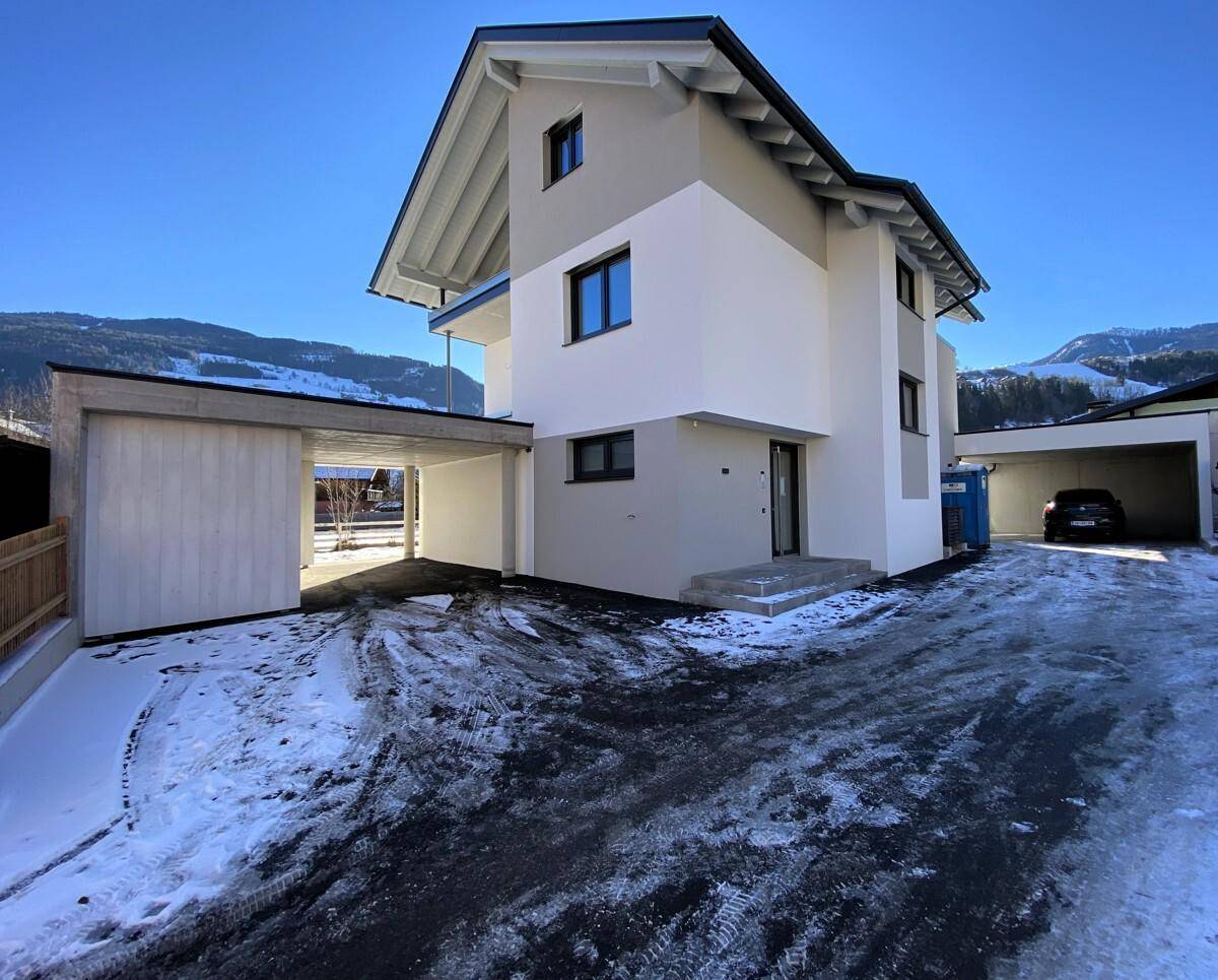 Modernes Einfamilienhaus mit Carport und verschneiter Auffahrt in den Bergen.