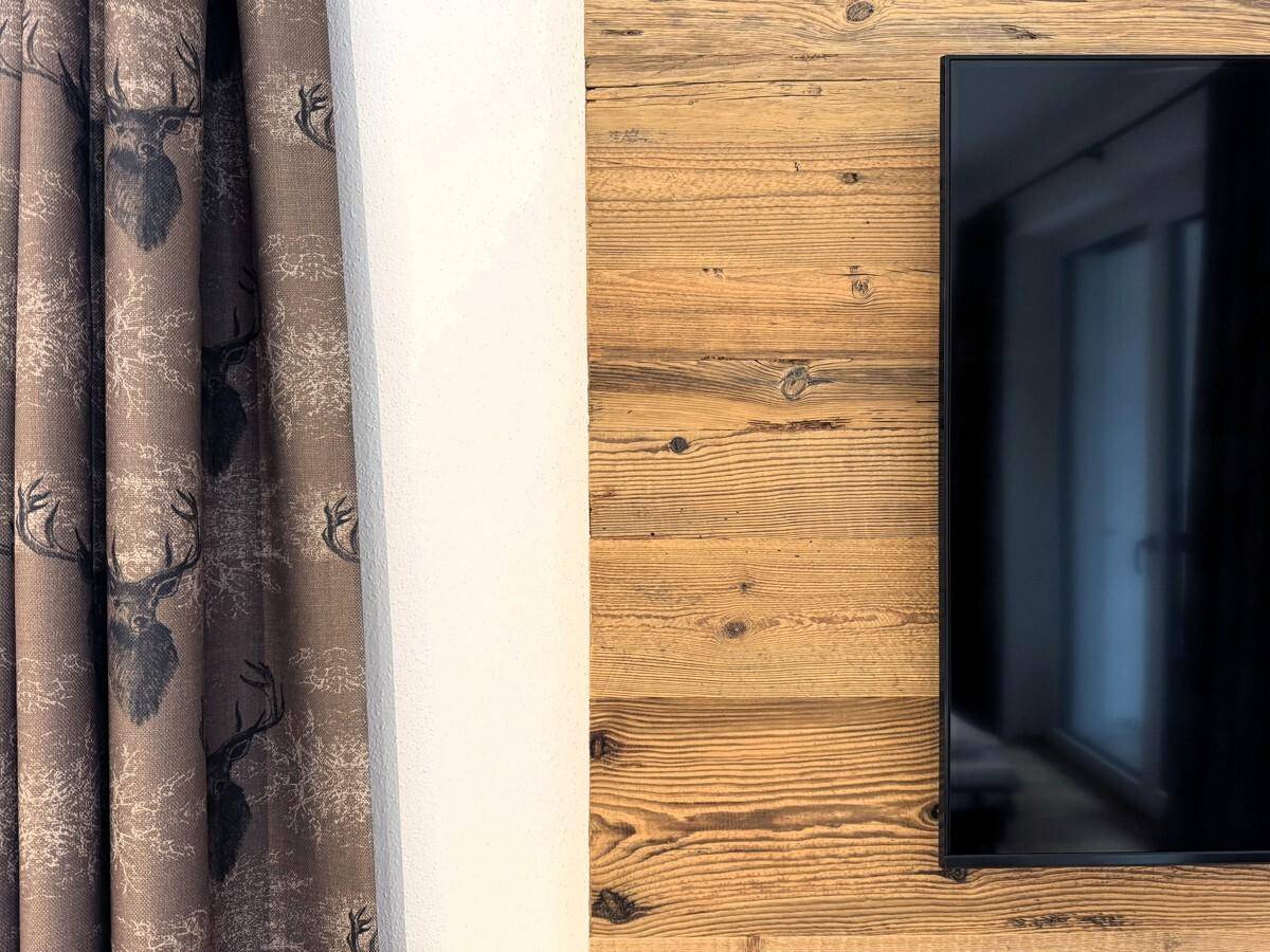 Detailansicht des Vorhangs mit Hirschmotiv und der Holzwandverkleidung im Schlafzimmer.
