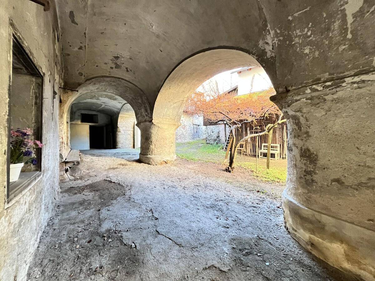Historischer Innenhof mit mehreren Bögen und einem unbefestigten Bereich, der zu weiteren Gebäudeteilen führt.