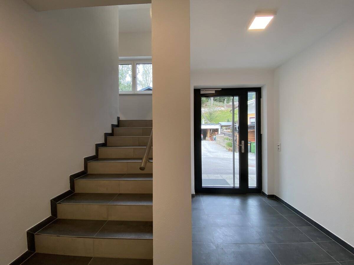 Heller Eingangsbereich mit Treppe, Fliesenboden und Zugang zum Außenbereich.