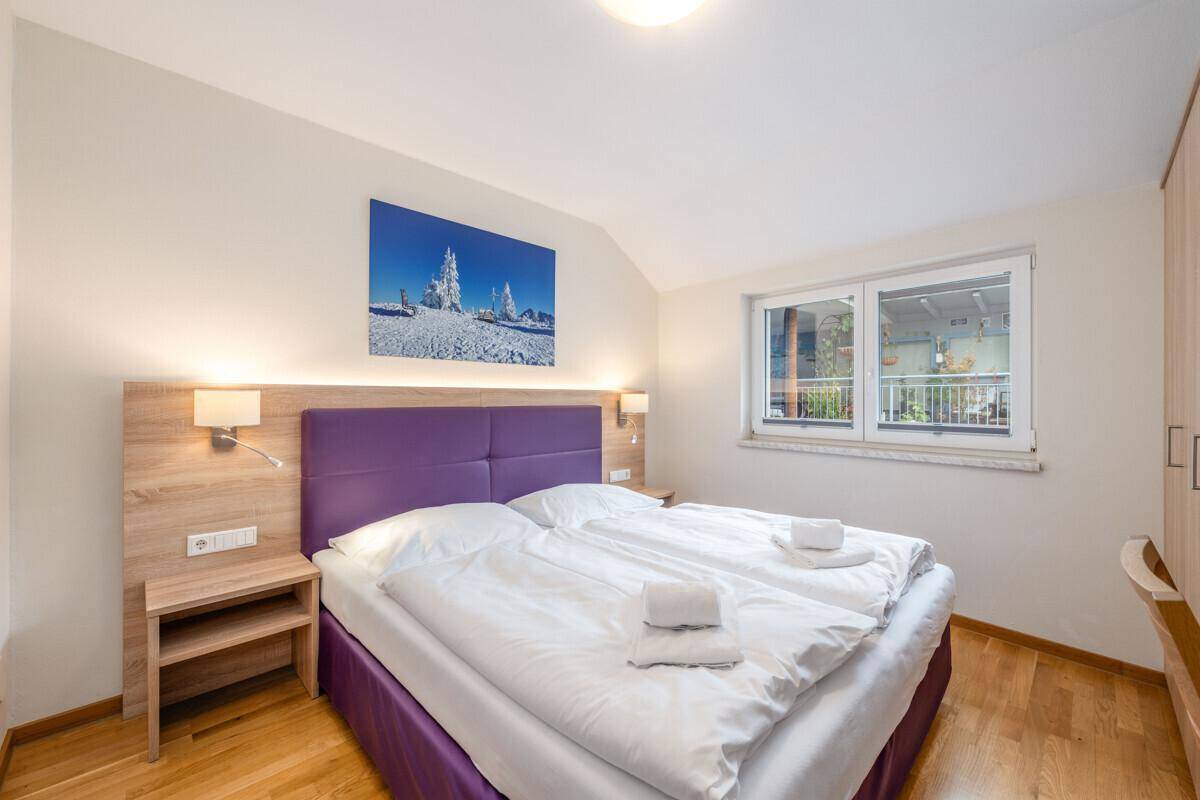 Schlafzimmer mit Doppelbett, Nachttischen, Kleiderschrank und Fenster mit Blick nach draußen.