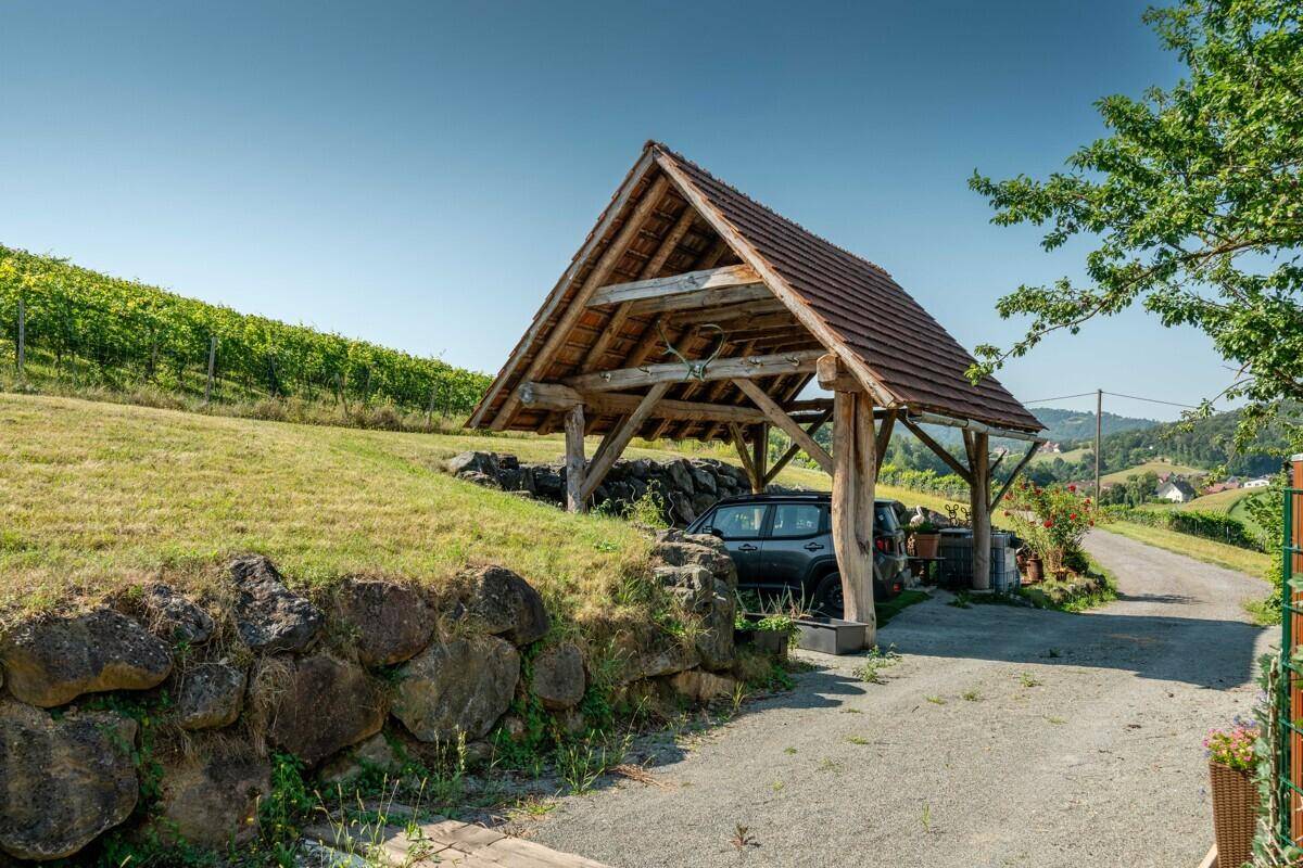 Rustikaler Holz-Carport neben einer Steinmauer mit Blick auf die umliegenden Weinberge.
