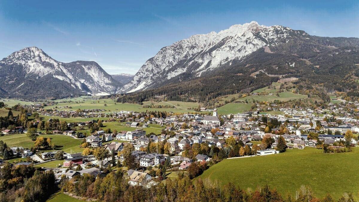 Malerisches Dorf in einem Tal, umgeben von majestätischen Bergen unter blauem Himmel.