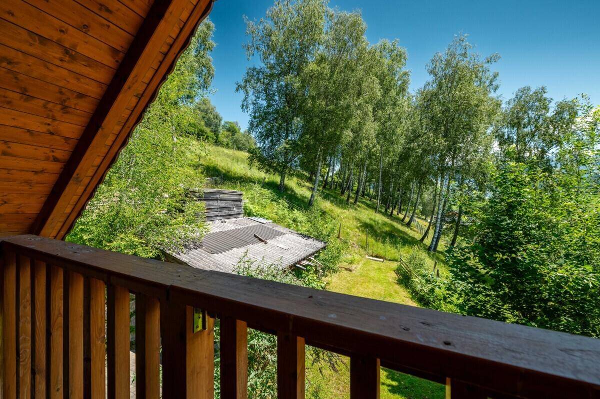 Blick von einem kleinen Balkon auf Bäume und eine grüne Hügellandschaft.