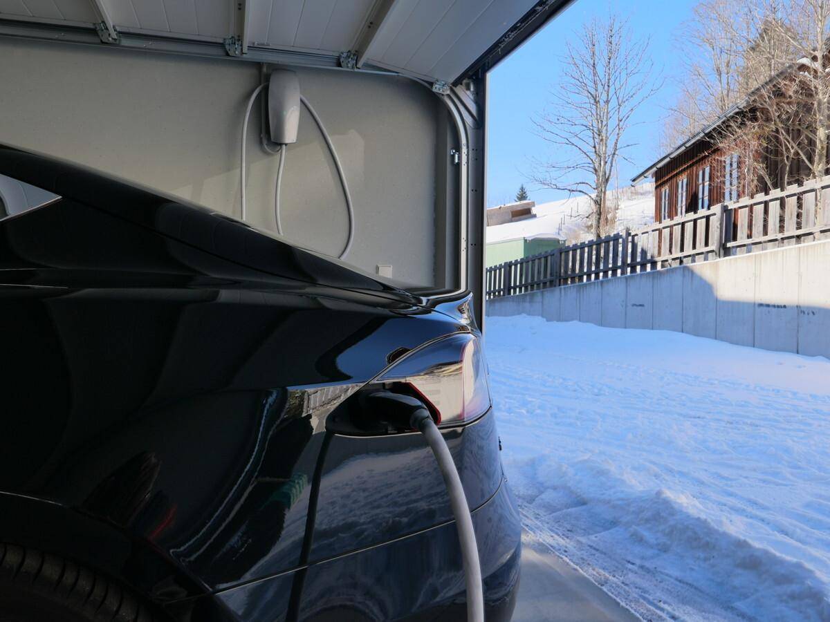 Blick aus der Garage mit einem ladenden Elektrofahrzeug und der verschneiten Außenumgebung.
