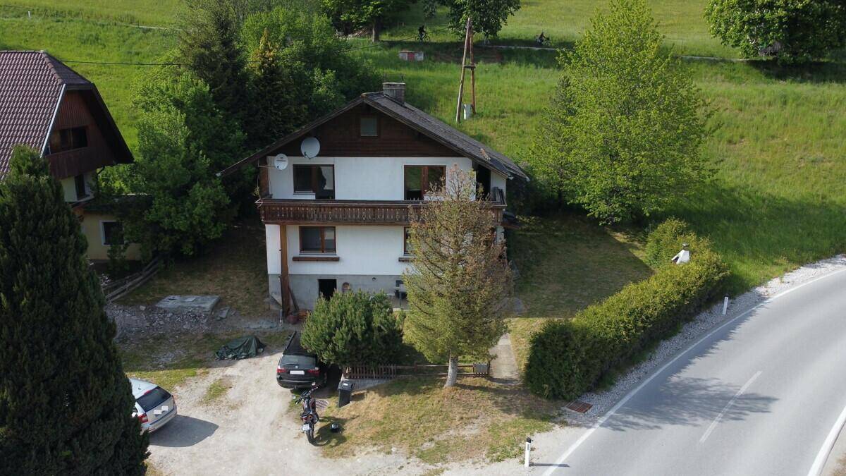Ländliches Wohnhaus mit Balkon und Satteldach, umgeben von viel Grün und einer Zufahrt.
