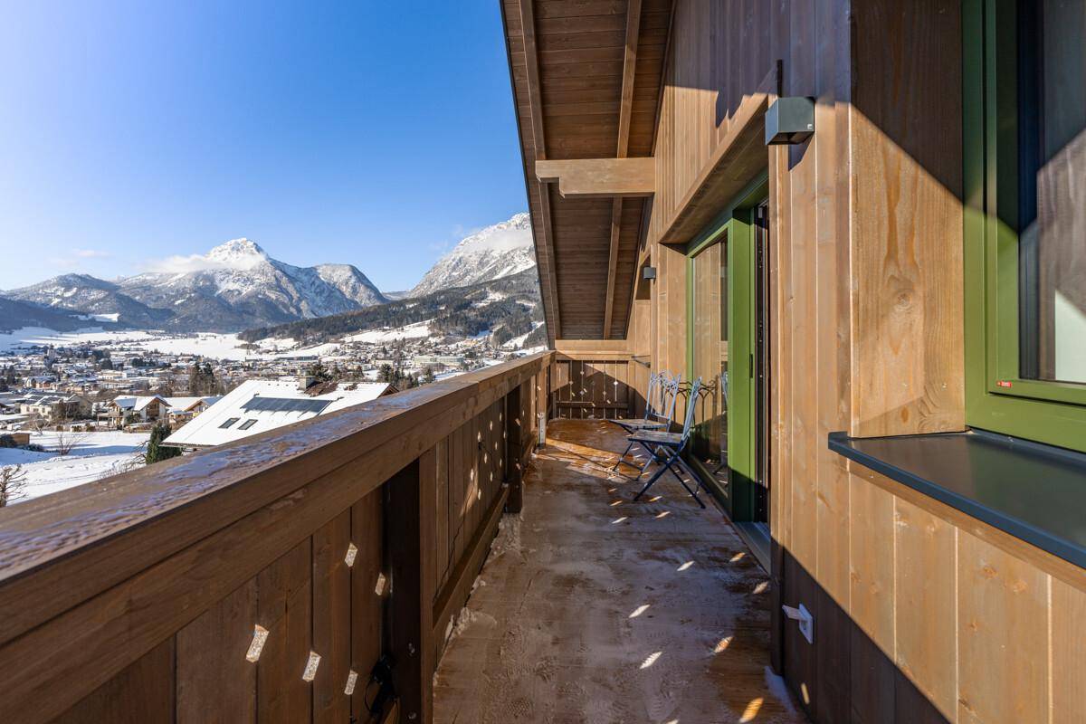 Langer Holzbalkon entlang der Fassade mit Sitzgelegenheiten und weitem Bergblick.