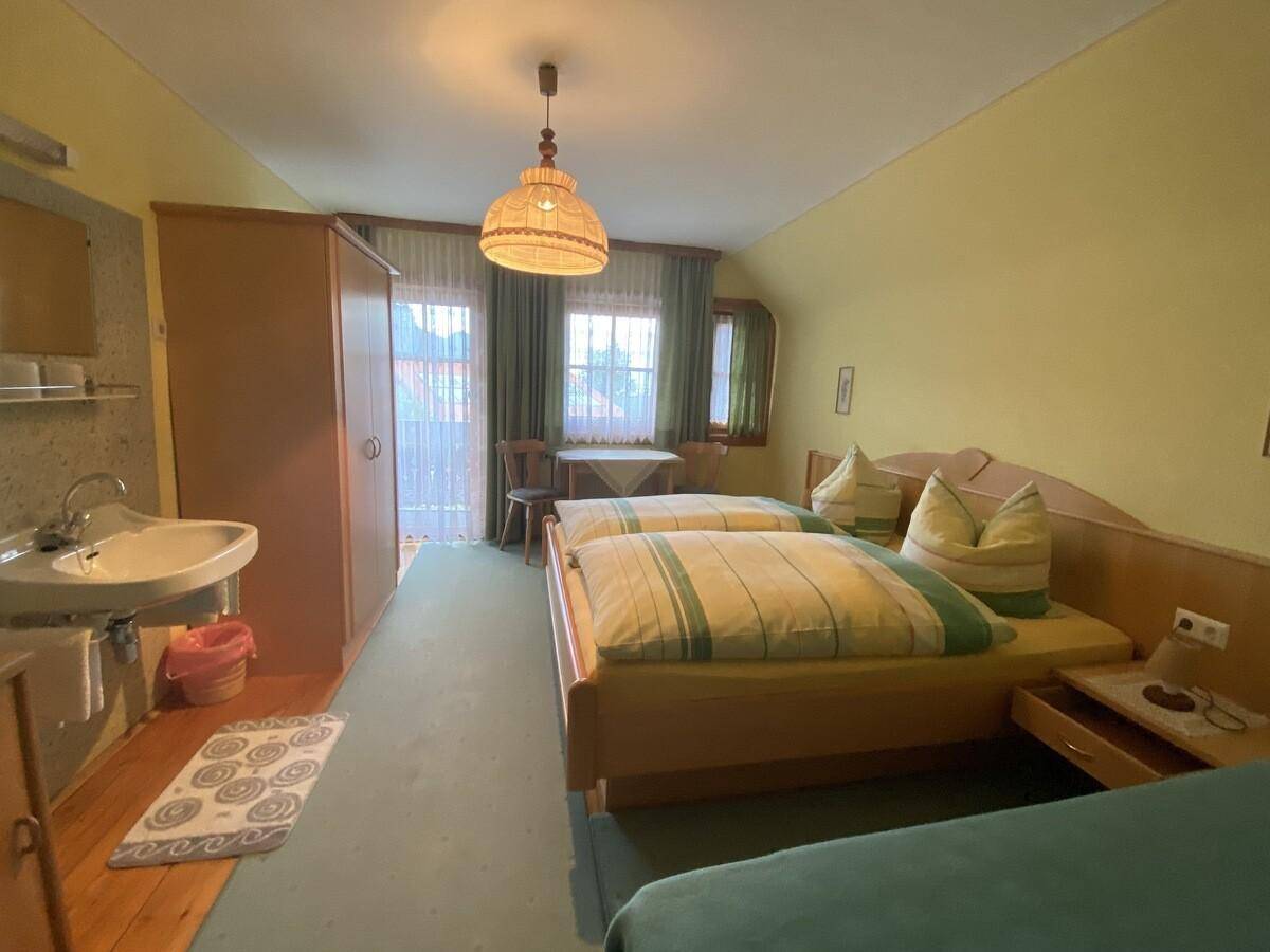 Helles Schlafzimmer mit drei Betten, integriertem Waschbecken und Zugang zu einem Balkon.
