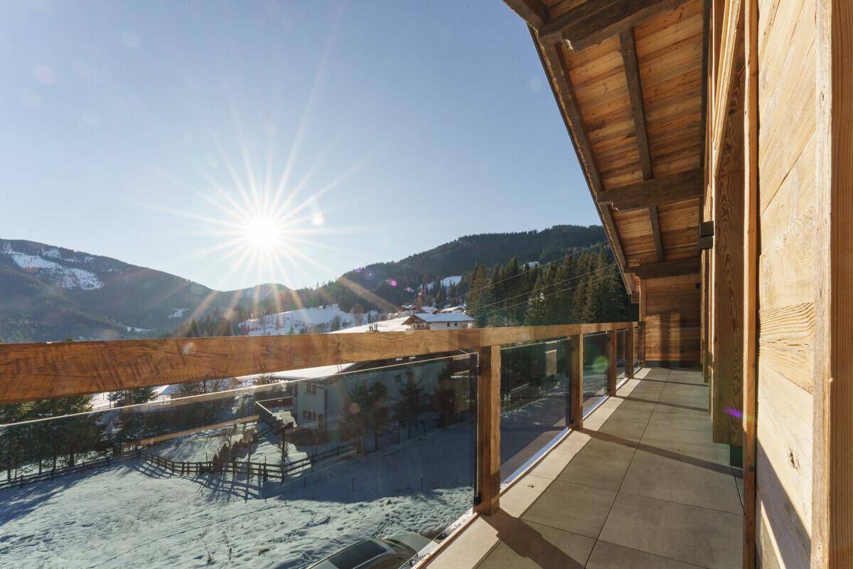 Sonniger Balkon mit Glasgeländer und weitem Blick auf die verschneite Berglandschaft.