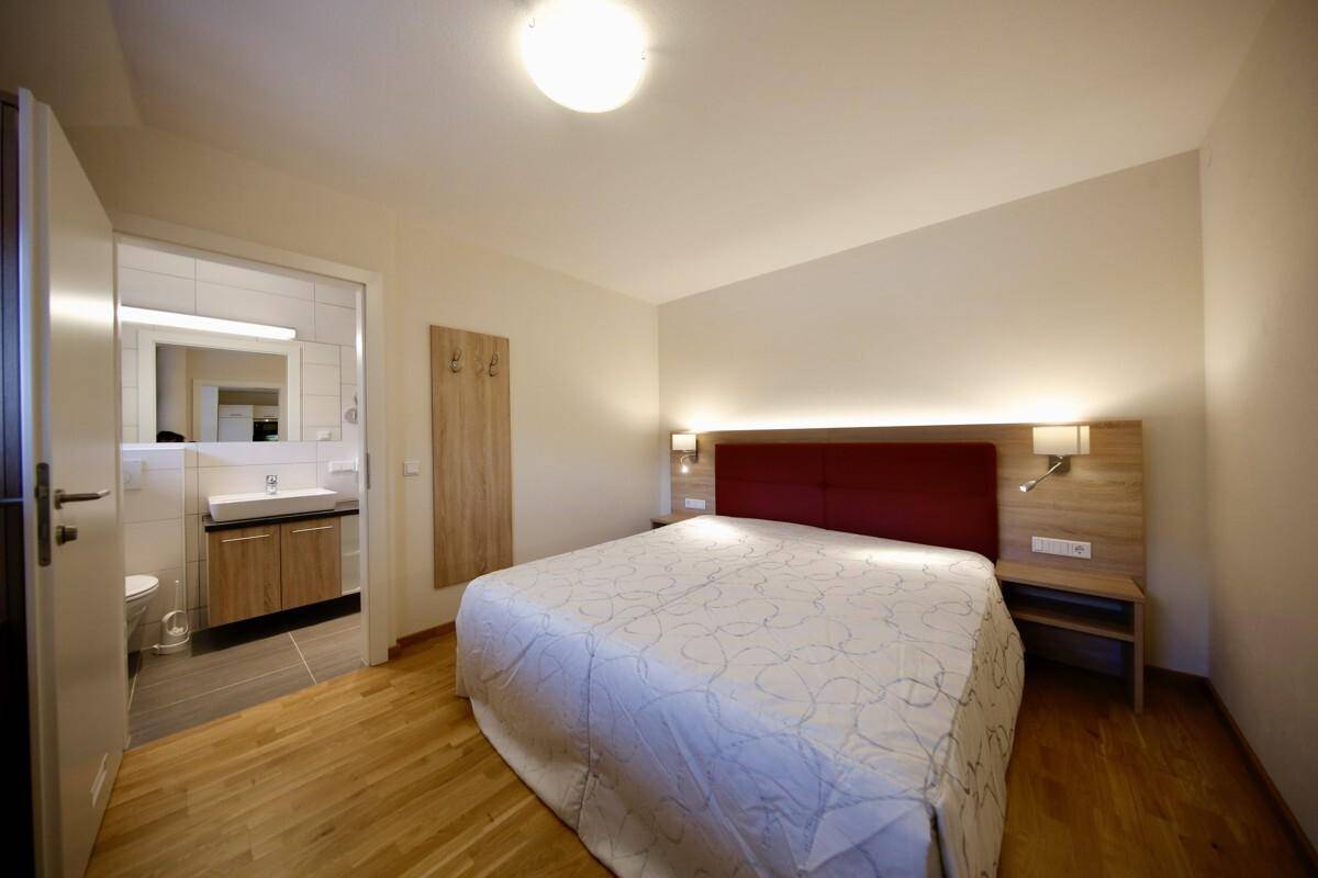 Schlafzimmer mit direktem Zugang zu einem Badezimmer, ausgestattet mit Waschbecken und wandhängender Toilette.
