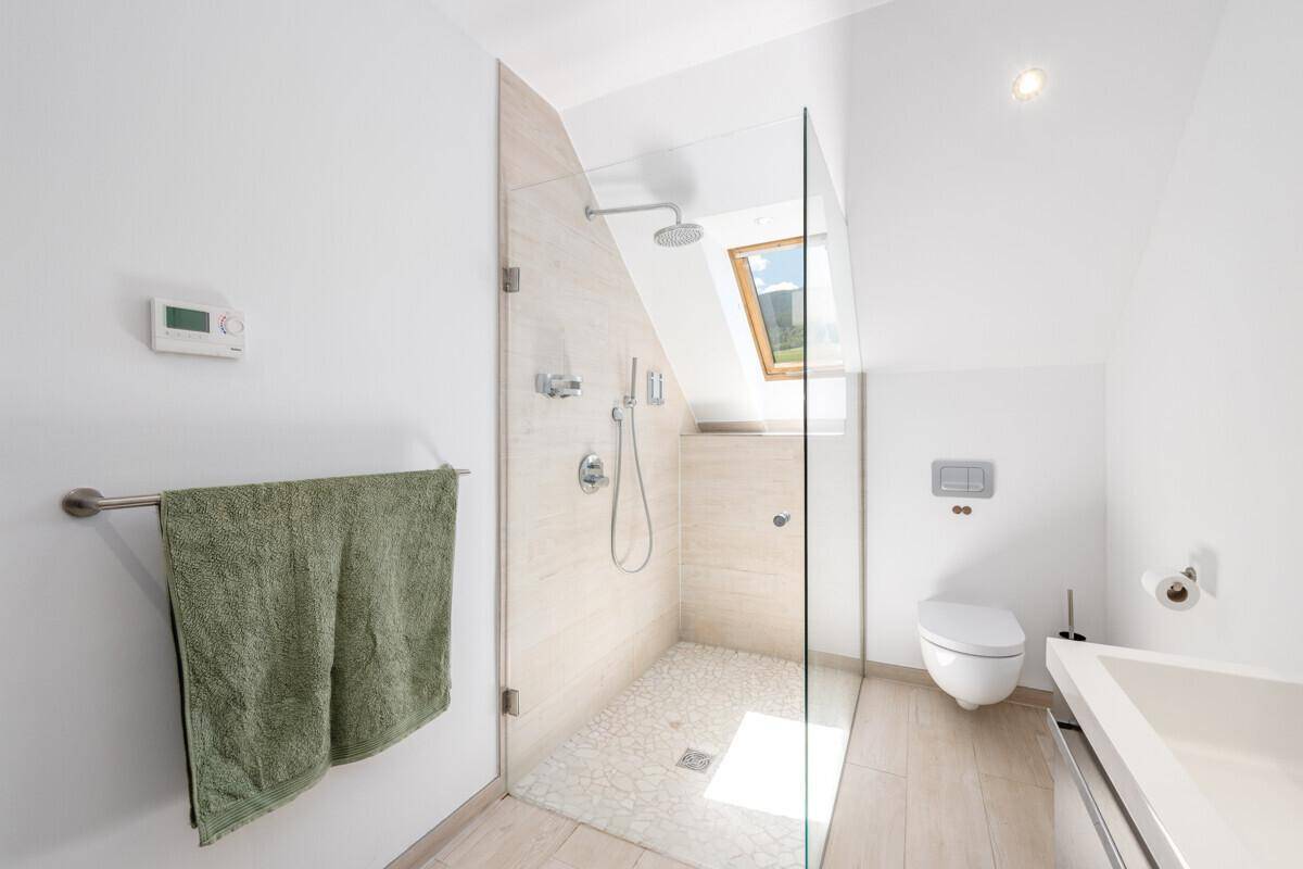 Helles Badezimmer im Dachgeschoss mit begehbarer Dusche, modernen Fliesen und Dachfenster.