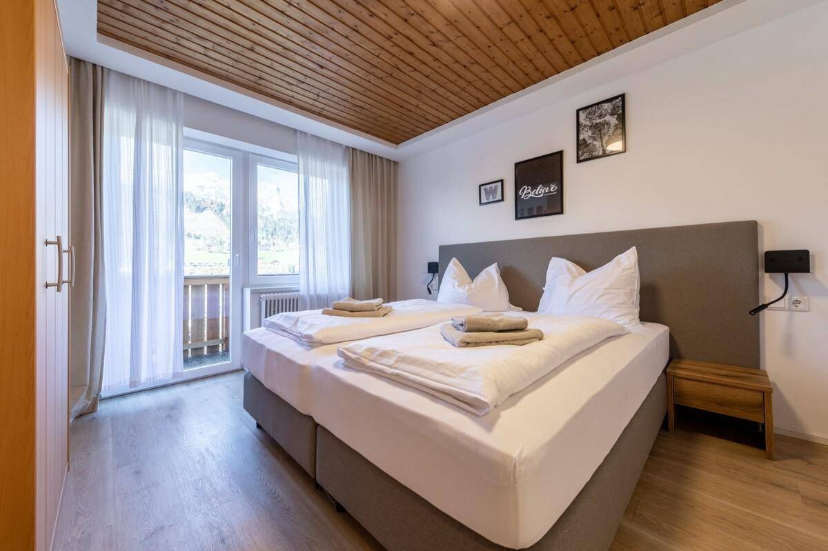 Gemütliches Schlafzimmer mit Doppelbett, Holzdecke und Zugang zu einem kleinen Balkon.
