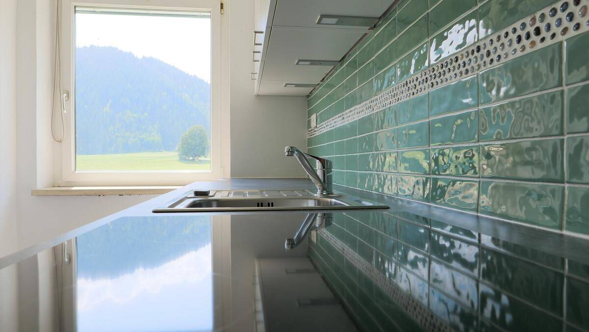 Küchenarbeitsplatte mit Spüle, grünen Fliesen und Ausblick ins Grüne durch das Fenster.