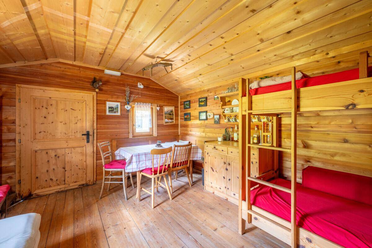 Rustikaler Wohn-Essbereich in einer Holzhütte mit Esstisch und Etagenbetten.