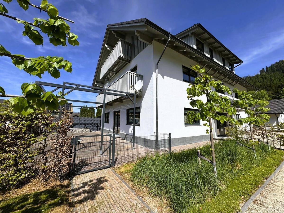 Modernes Gebäude mit weißer Fassade, Balkonen und grüner Umgebung.