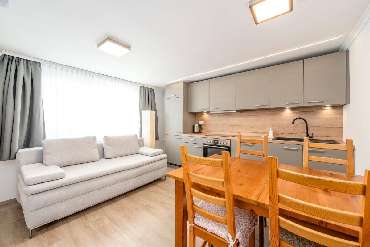 Heller Wohn-Essbereich mit integrierter Küchenzeile, Holztisch und bequemer Couch.