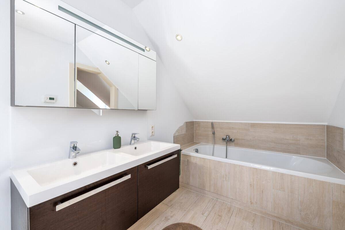 Modernes Badezimmer im Dachgeschoss mit Doppelwaschbecken, Badewanne und Spiegelschrank.