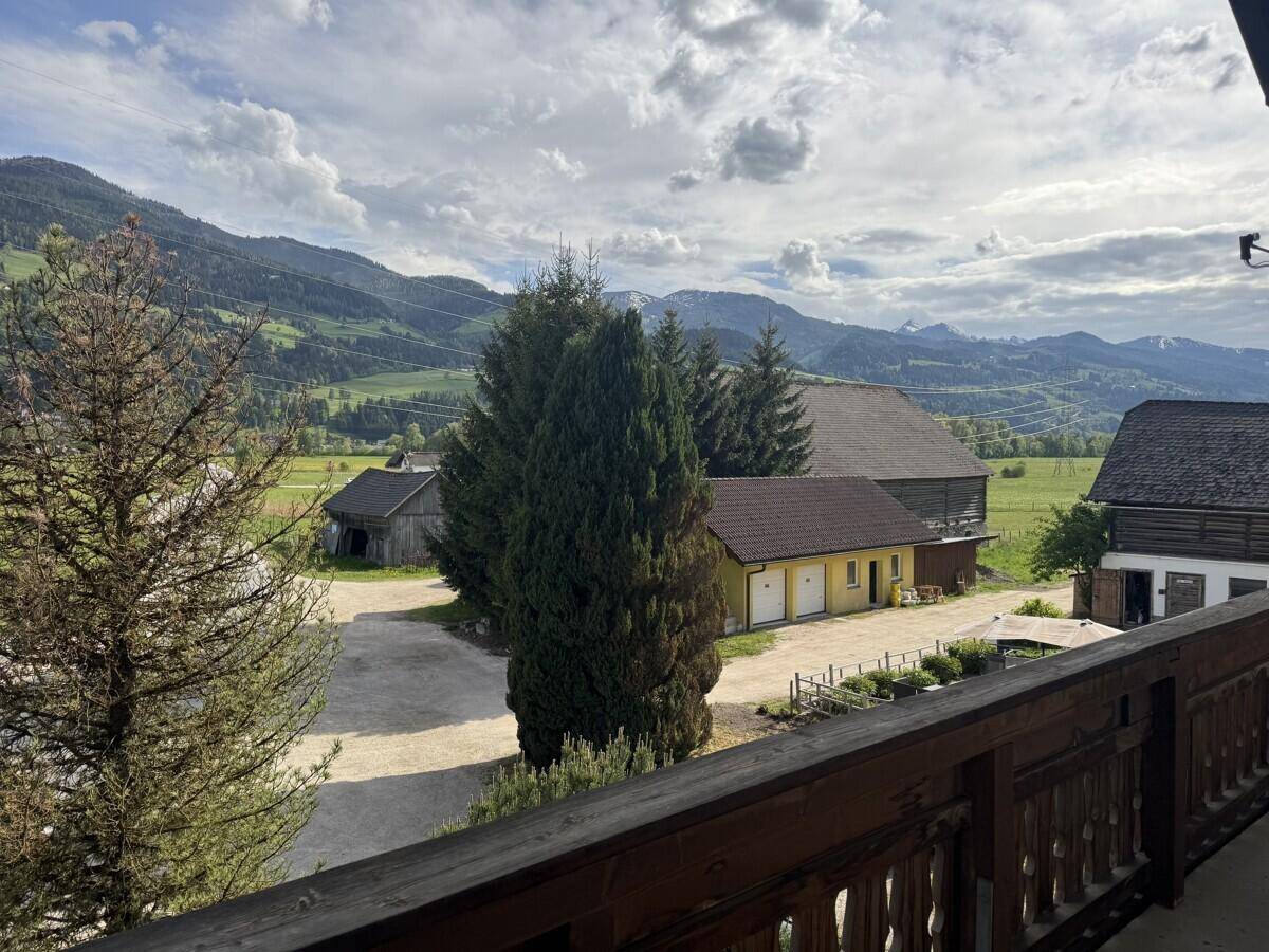 Blick vom Balkon auf umliegende Gebäude, einen Hof und die beeindruckende Bergkulisse.