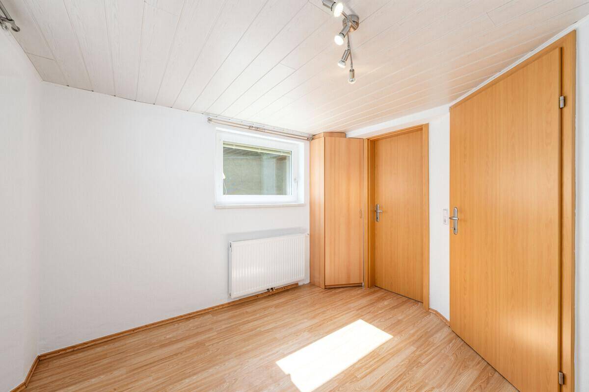 Helles Zimmer mit Holzboden, weiß gestrichenen Wänden und Deckenpaneelen.